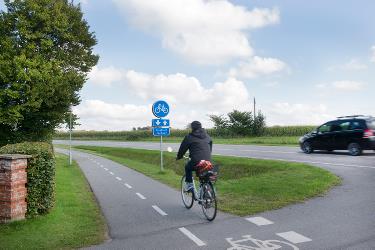 Cyklist der cykler på dobbeltrettet cykelsti langs hovedvej. 